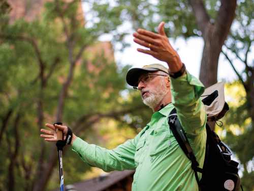 Peter Wampler wears hiking gear and stands and lectures to students outside